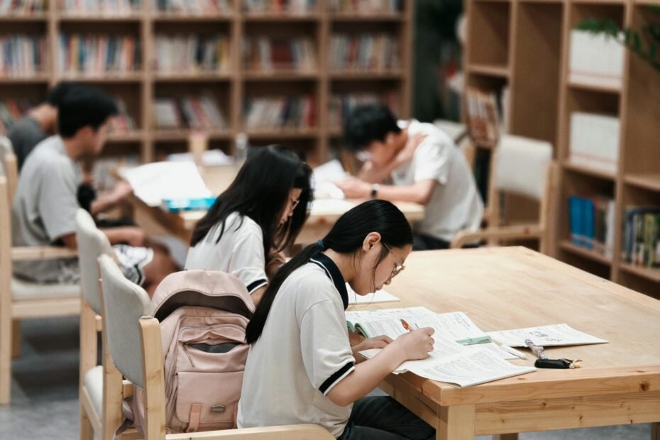 Group of students focused on studying inside a library, surrounded by bookshelves.