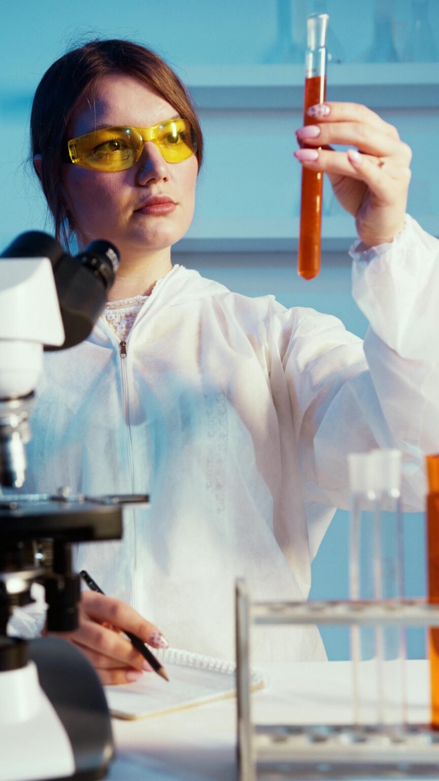 A female scientist in protective gear analyzing a test tube in a laboratory setting.